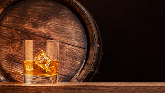 Glass of whiskey over ice in front of an aged oak barrel